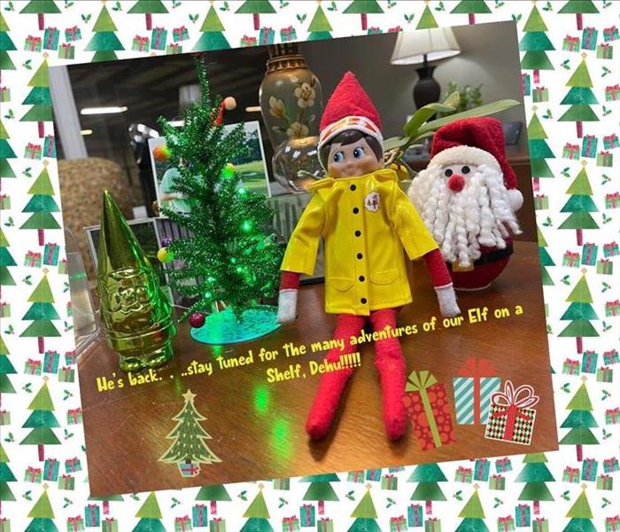 Photo of our elf on the shelf named Dehu with text overlay stating he's back and to stay tuned.